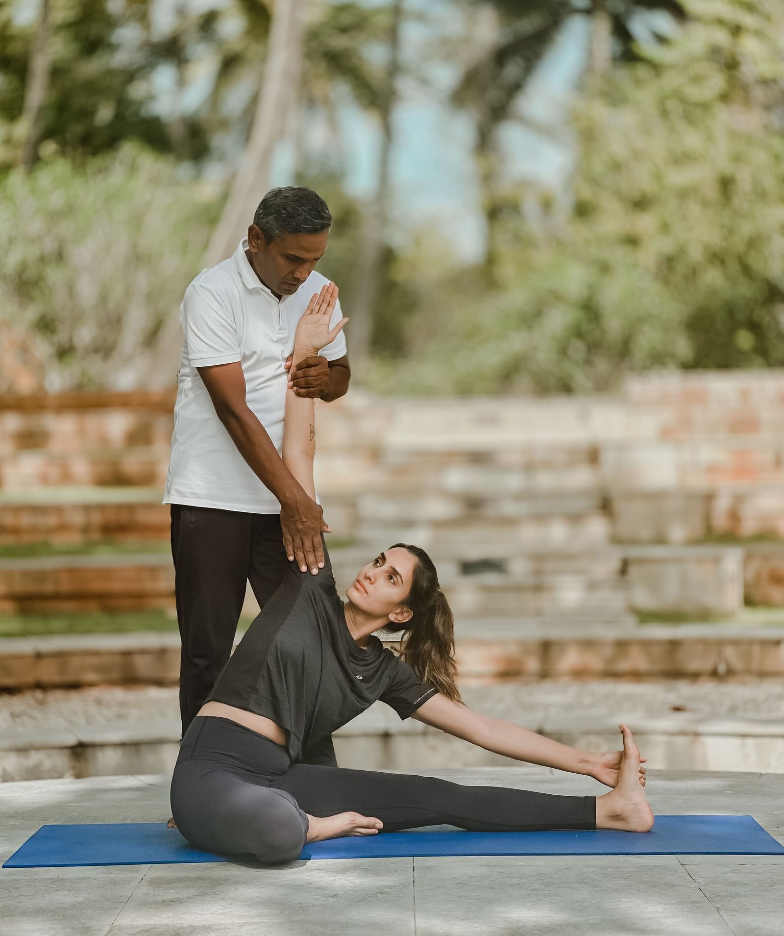 People doing yoga poses outdoors, stone steps, trees in background - Shreyas Retreat