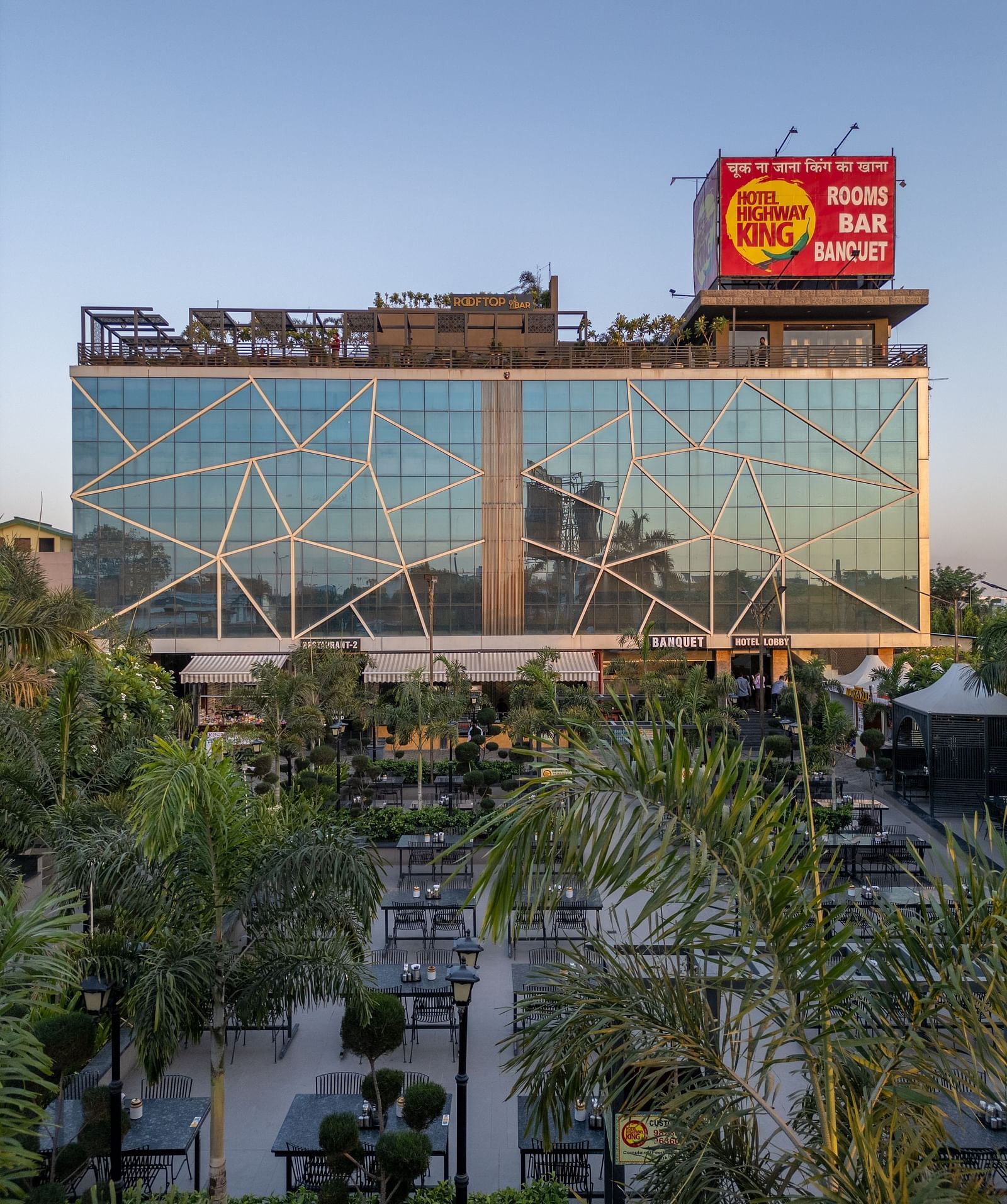 Exterior view of Hotel Highway King with glass facade and signage, surrounded by green trees.