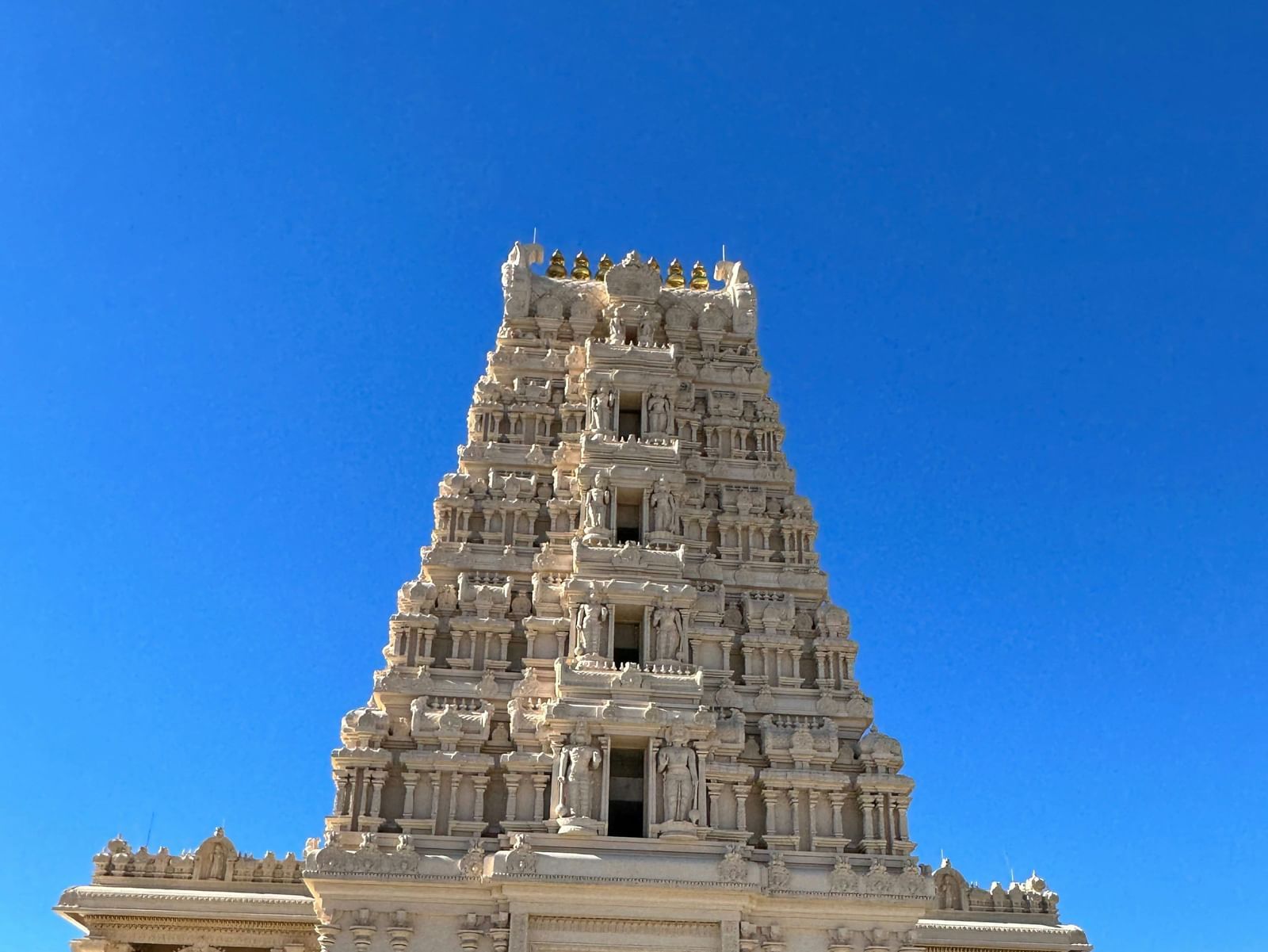 A large, modern-looking white temple building with a detailed tower structure under a clear blue sky.