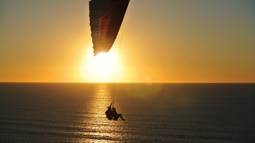 A view of a person parasailing with the setting sun in the background.