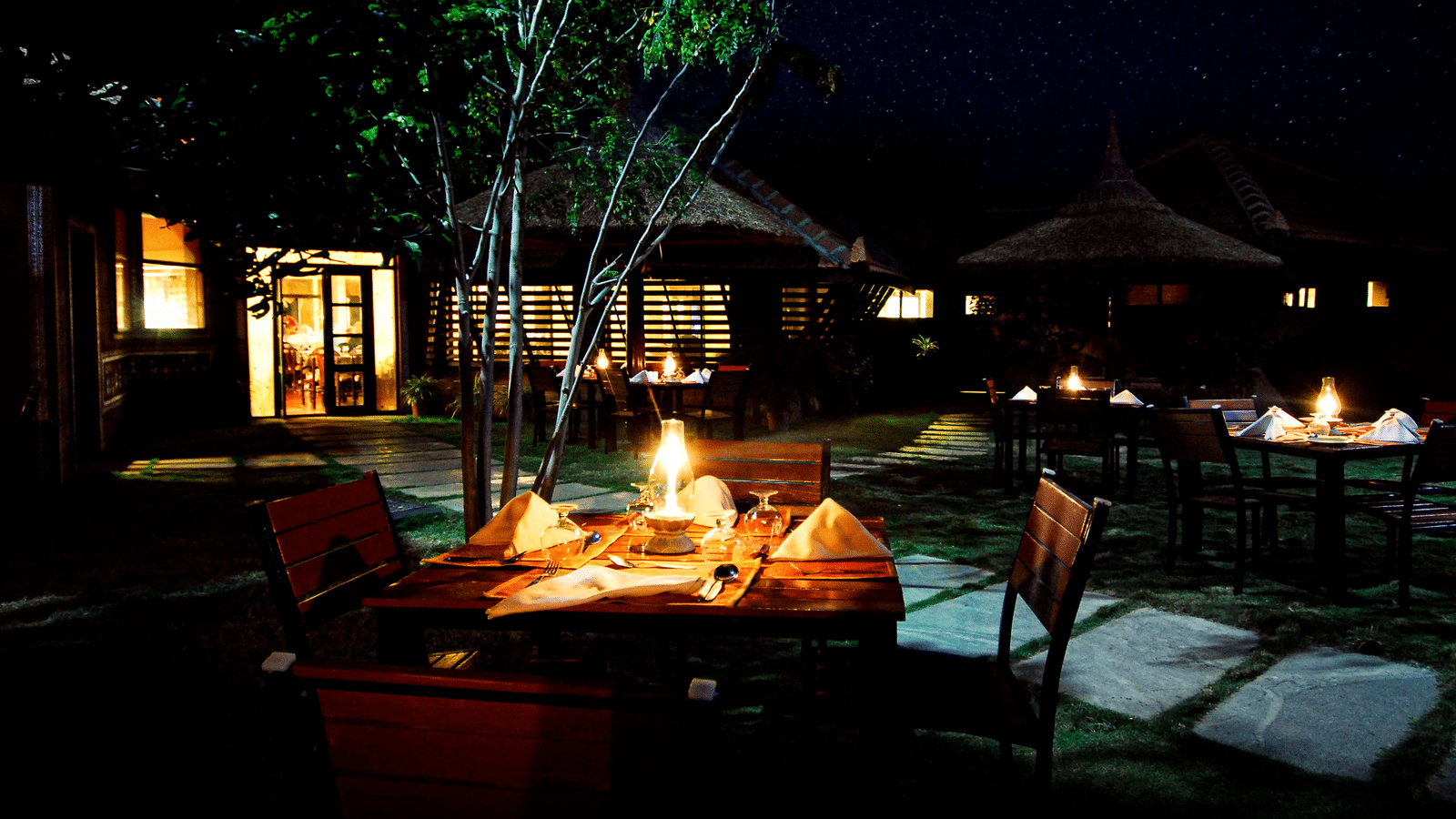 A candle light dinner table set in the garden at night at Hoysala Village Resort, Hassan offering unique stays in Karnataka