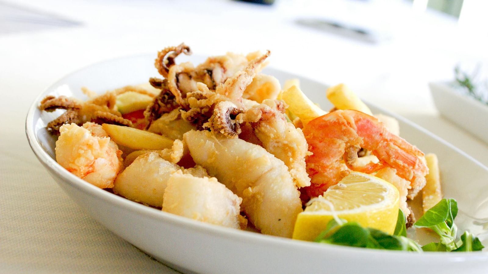 Deep fried shrimp and squid with a slice of lemon on a ceramic plate.