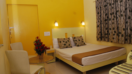 A well-lit hotel room featuring a double bed with patterned pillows, bright yellow walls, and a small sitting area with a coffee table - Hotel Pandian