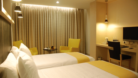 A room with seating area, twin beds and a television in front at The Oriental Residency.