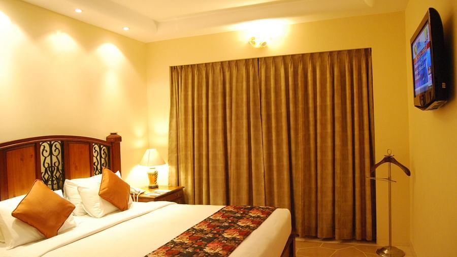 A king bed with a large mattress and cushions, facing a flatscreen TV in a well lit room