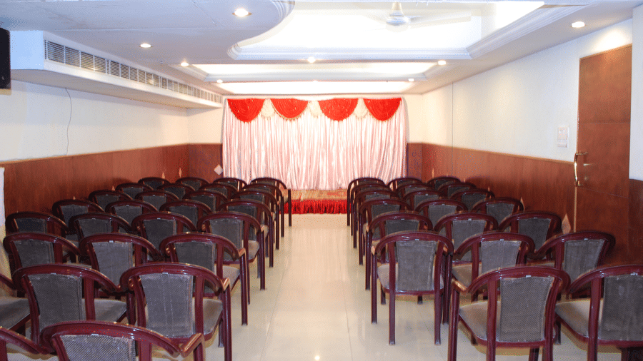 A long event or banquet hall set up with rows of chairs facing a stage decorated with red and white drapes.