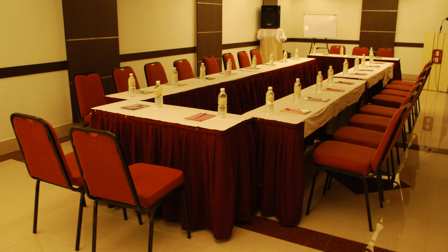 A conference room arranged in a U-shaped layout with white tablecloths and red padded chairs - Hotel Pandian