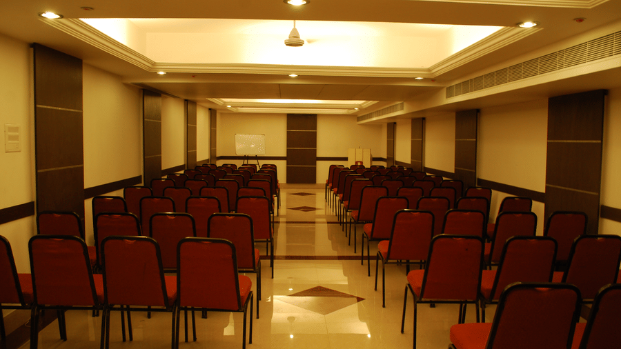 An empty seminar hall with rows of red chairs set up in a theatre-style arrangement for a presentation - Hotel Pandian