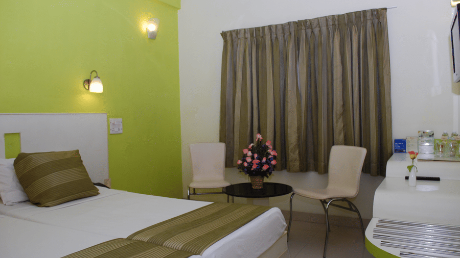 Hotel bedroom interior with adjoined twin beds, a light green accent wall, and a small coffee table seating arrangement - Hotel Pandian