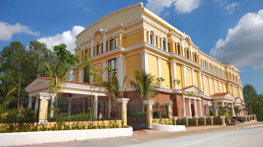 An image of a hotel with an elegant entrance gate, small shrubs lining the pathway, and a lush garden in the foreground.