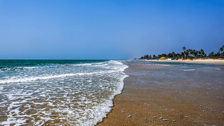 Foamy Waves flowing over the shoreline at Varca Beach with beach umbrellas and trees in the background. Visiting this beach is one of the best things to do in Varca, Goa.