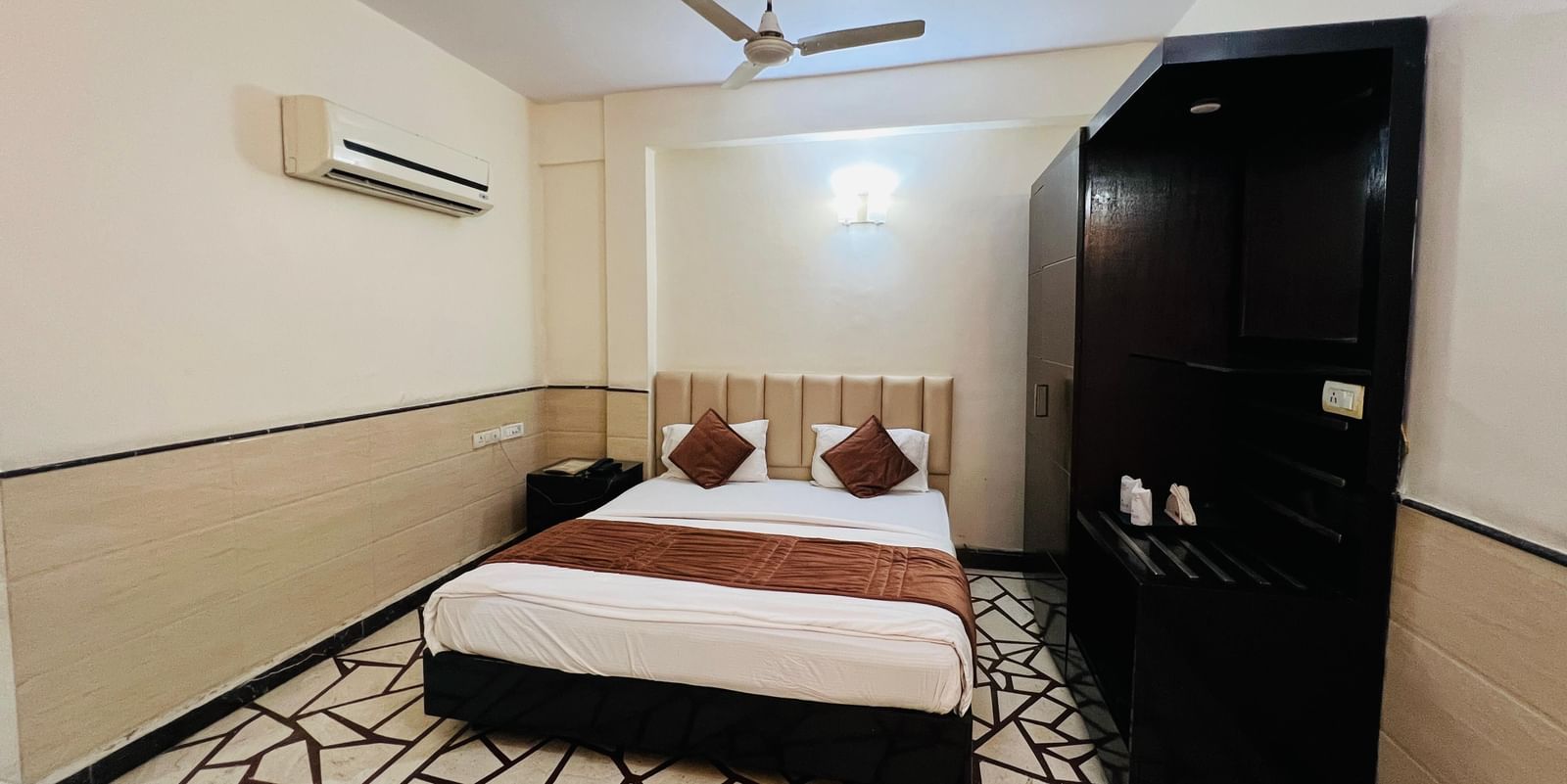 A well-furnished hotel room featuring a comfortable bed with red pillows and dark wood furniture, offering a restful stay. | Suite | Hotel Aadhar