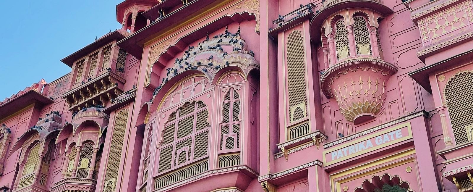 A grand, ornate pink palace with intricate architecture and arched windows, under a clear blue sky.
