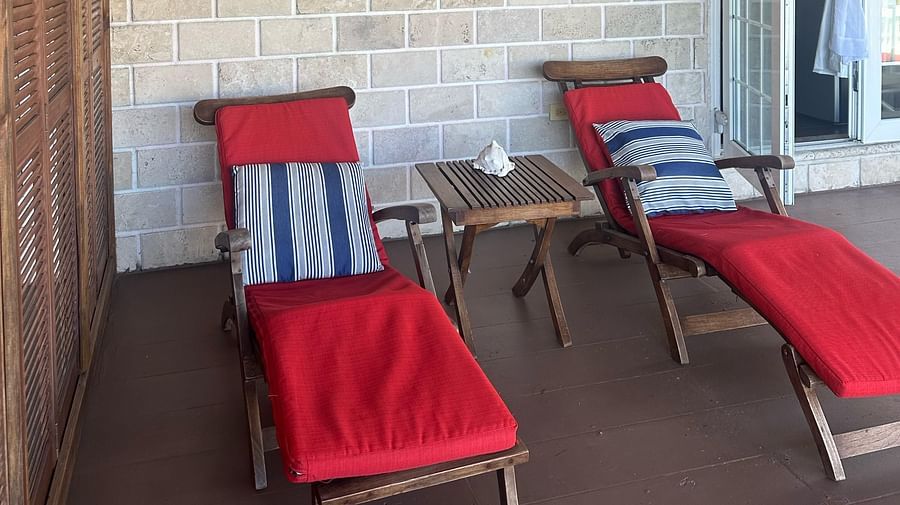 Covered porch with red lounge chairs and small tables outside a room | A Stone's Throw Away