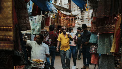 A narrow market street with hanging cloths, small shops on both sides, and people walking through.
