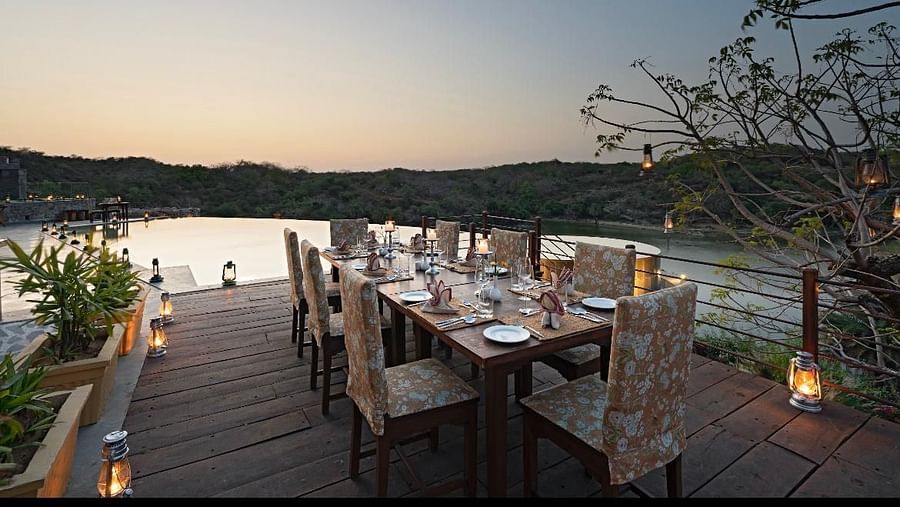 A dining table with chairs tucked inside placed on a wooden bridge near the lake