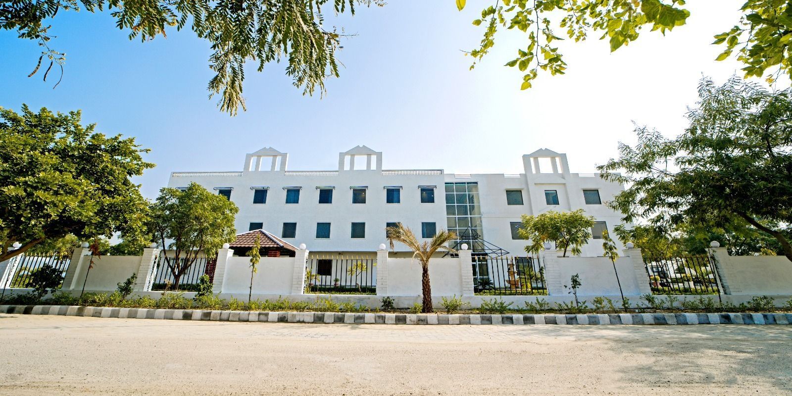Front view of Grassfield Riveria Resort, Jaipur, surrounded by trees and clear skies, showcasing the modern building facade.