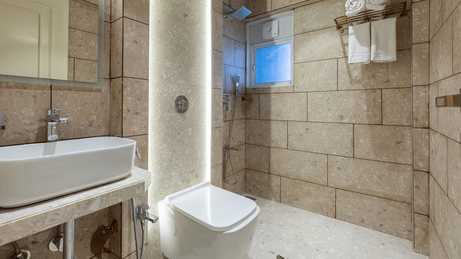 A clean bathroom with textured stone tiles, a white vessel sink, and a glass-enclosed walk-in shower - Home2 Residency, Mumbai Airport