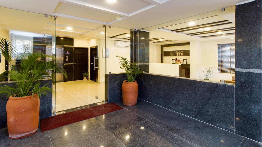 Hotel entrance with a checkered marble floor, glass doors, and a plant at Sanctum Suites Whitefield, Bangalore.