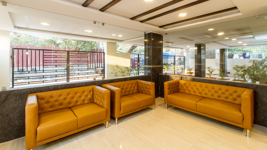 Bright hotel lobby with mustard leather sofas, a reception desk, and a striped ceiling at Sanctum Suites Whitefield, Bangalore.