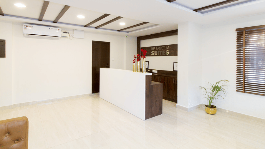 Hotel reception desk with bright white interiors, a striped ceiling, and a sofa at Sanctum Suites Whitefield, Bangalore.