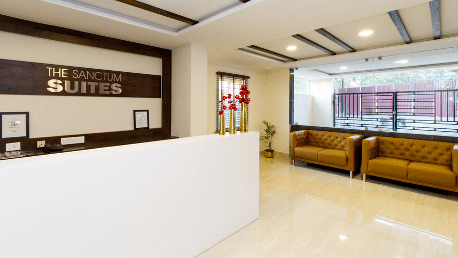 Hotel reception area with the Sanctum Suites signage, a mustard sofa, and a marble floor at Sanctum Suites Whitefield, Bangalore.