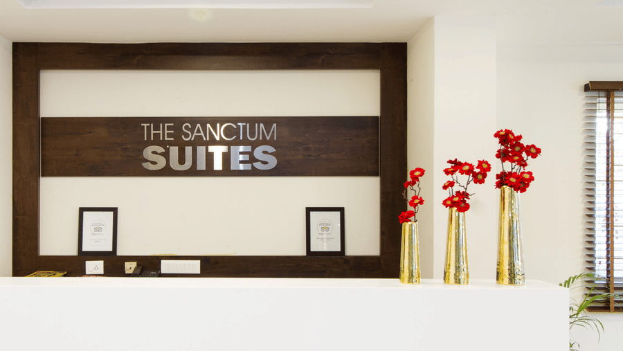 The Sanctum Suites branded wall with red floral arrangements and gold vases at Sanctum Suites Whitefield, Bangalore.