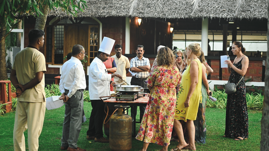 An overview of a group of women interacting with a chef during an outdoor cooking workshop at Ayur On The Beach Nattika.