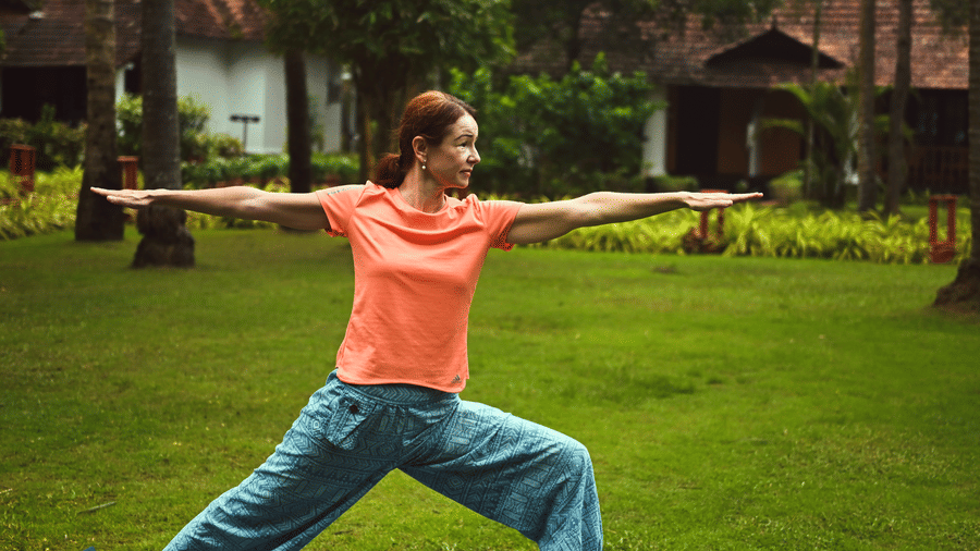 A woman practicing yoga on lawn area with villas in the background at Ayur On The Beach Nattika.