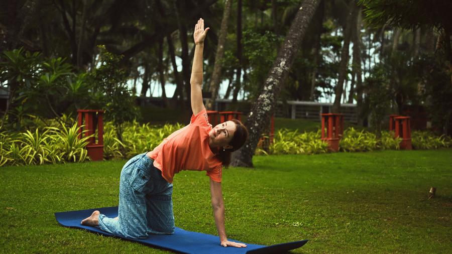 A women practicing a yoga pose on the lawn are with trees in the background at Ayur On The Beach Nattika.