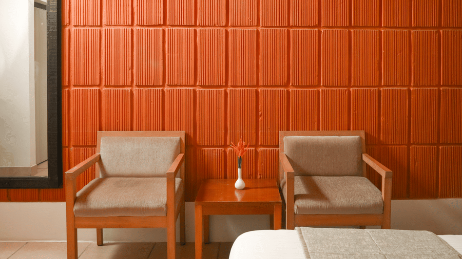 A seating area at Kadkani River Resort, Coorg featuring 2 armchairs, small square wooden table, textured wall and tiled floor.