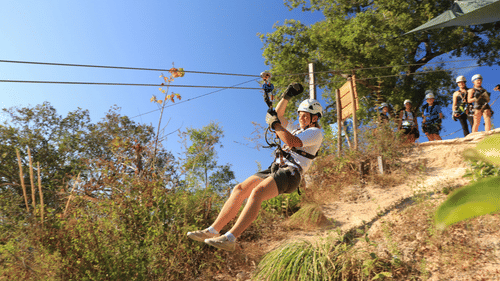 A boy ziplining on top of a lush green hillside