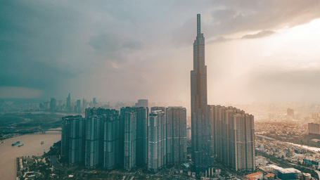 An aerial view of Ho Chi Minh City in Vietnam with many skyscrapers in view, including Landmark 81 building. The view captures sun light on one side and thunder storms on the other side.