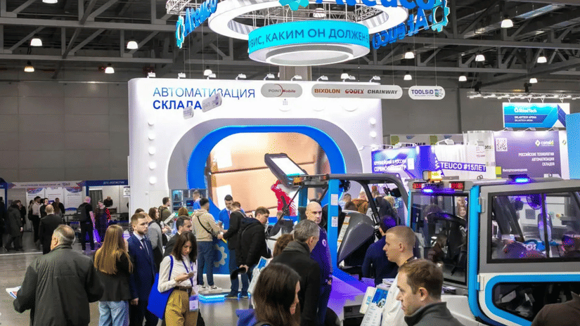 An overview of a trade fair with people surrounding booths and interacting with other people.