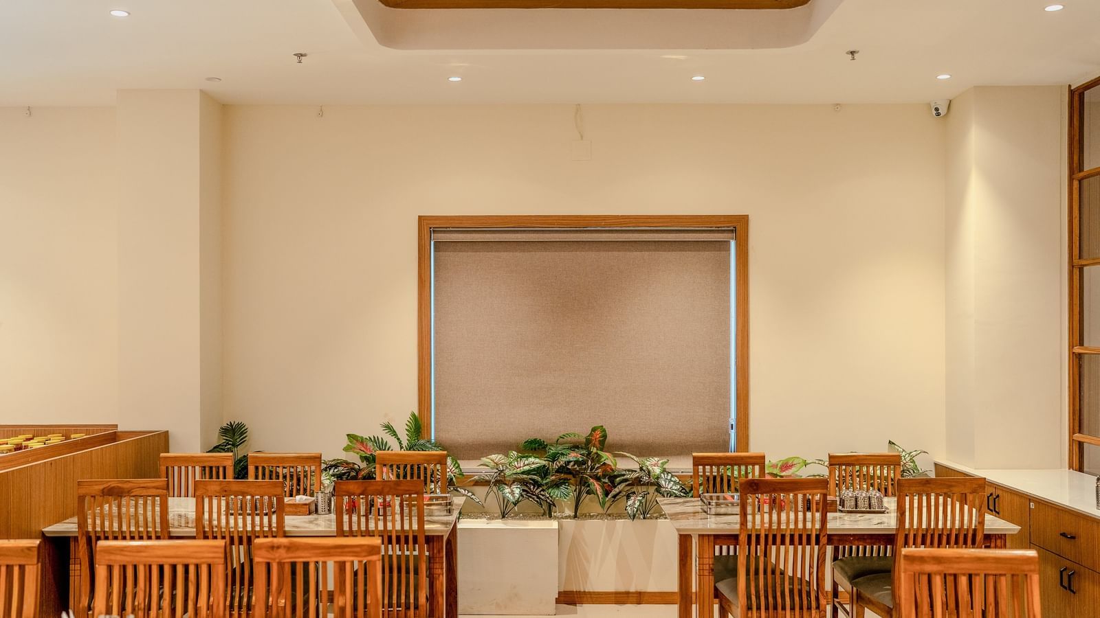 A window with brown-coloured blinds covering it along with well-arranged dining setup at Daksh The Grand Goverdhan, Dwarka.