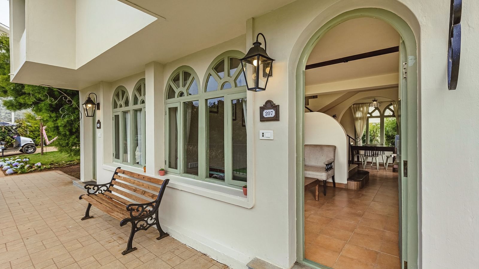 Exterior view of Mango Hill Shola, Ooty, showcasing arched windows, a structured façade, and a bench along the entrance walkway.