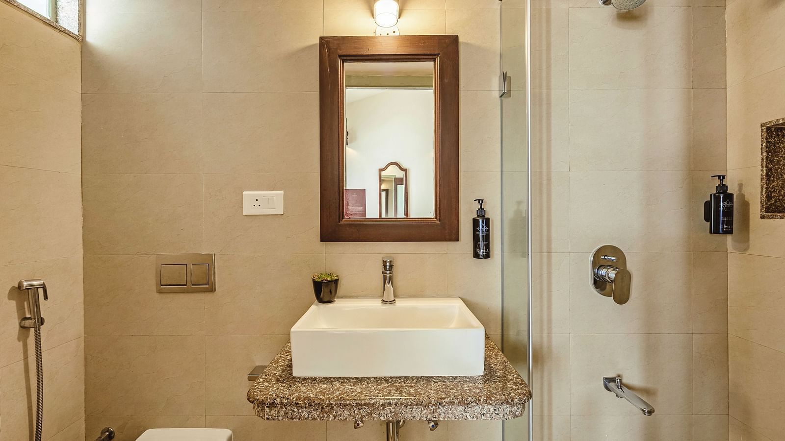 Stylish bathroom at Mango Hill Shola, Ooty, equipped with a modern sink, wall-mounted mirror, and western-style toilet, all under soft ambient lighting.