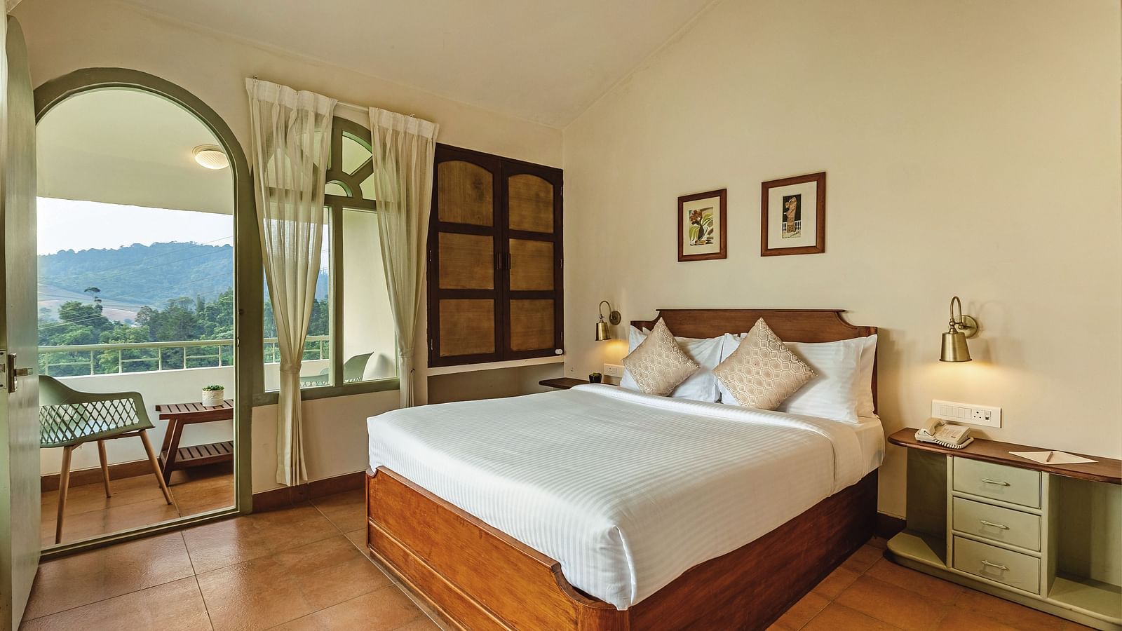 Comfortable bedroom at Mango Hill Shola, Ooty, with a plush double bed, bedside lamps, and an arched window that opens up to serene landscape views.