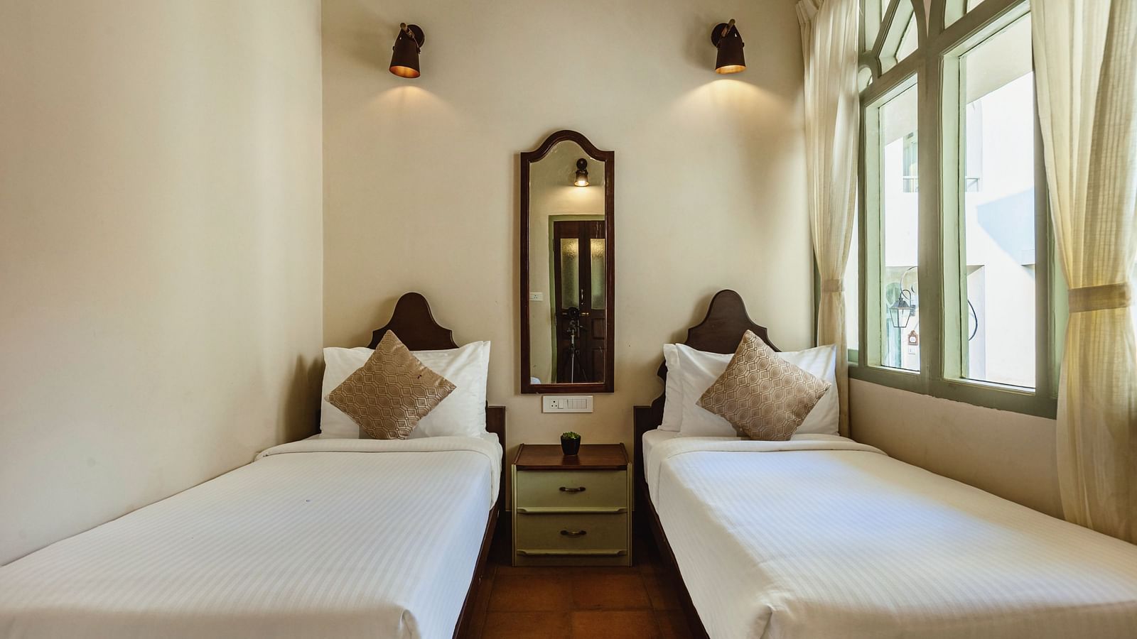 Twin bedroom at Mango Hill Shola, Ooty, with two single beds, bedside lamps, and windows providing daylight.