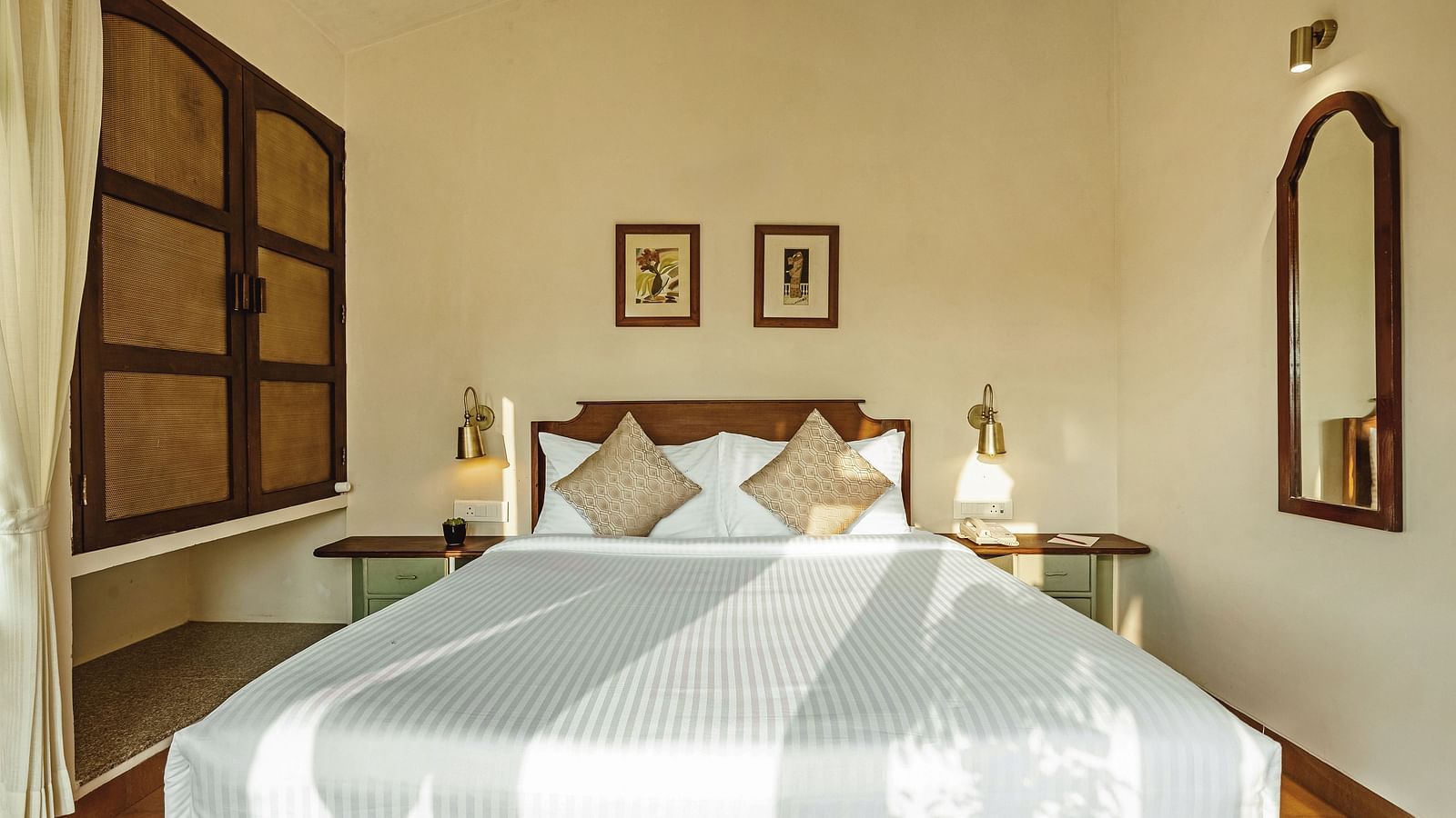 Bedroom at Mango Hill Shola, Ooty, with a double bed, striped bedding, bedside tables, and framed pictures on the wall.