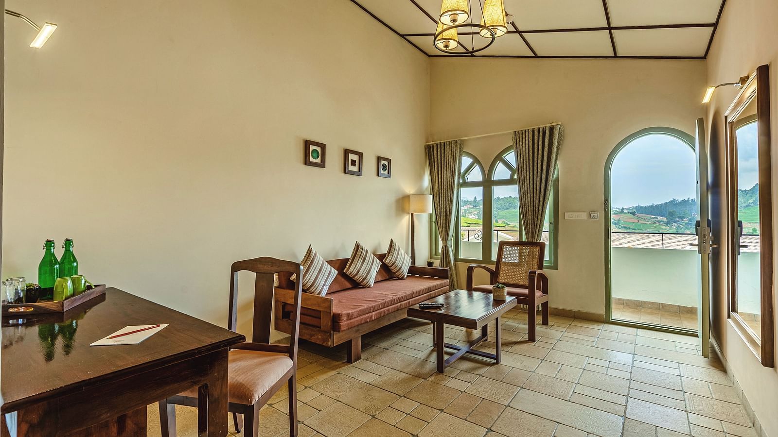Bright room at Mango Hill Shola, Ooty with a writing desk, refreshments, and large arched doors opening to scenic views.