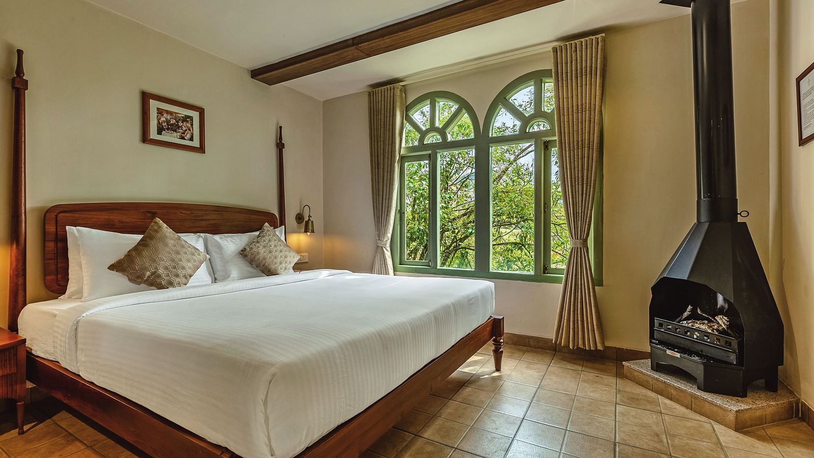Junior Suite with Bathtub at Mango Hill Shola, Ooty with a canopy bed, fireplace, and large arched window framing scenic greenery.