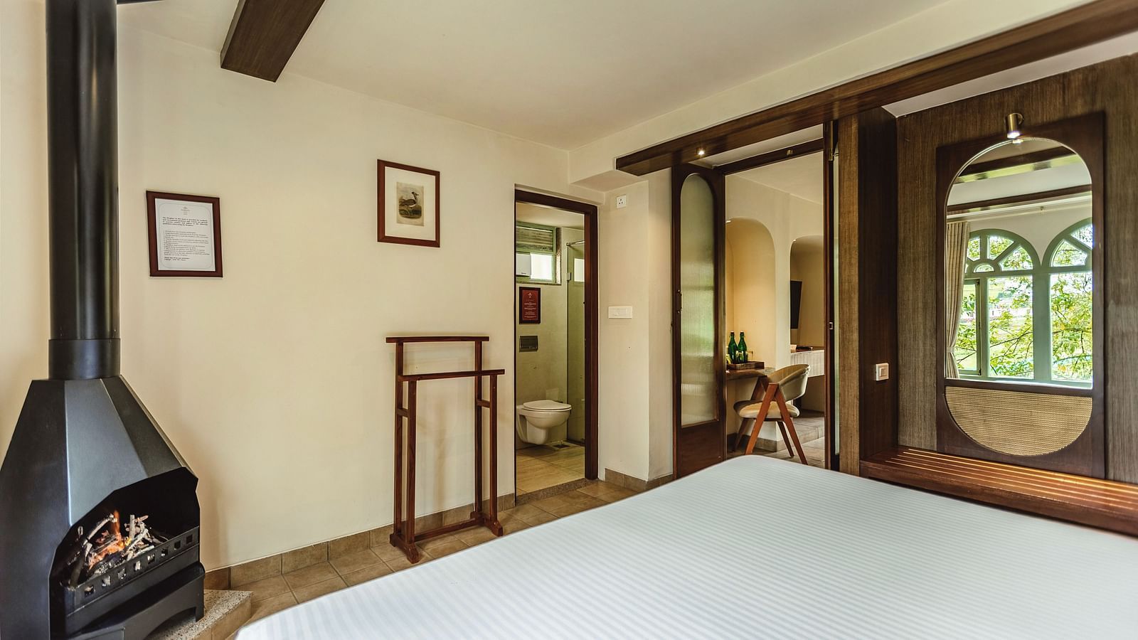 Rustic-style bedroom with a central fireplace and a large mirror reflecting the charming interiors of Mango Hill Shola, Ooty.