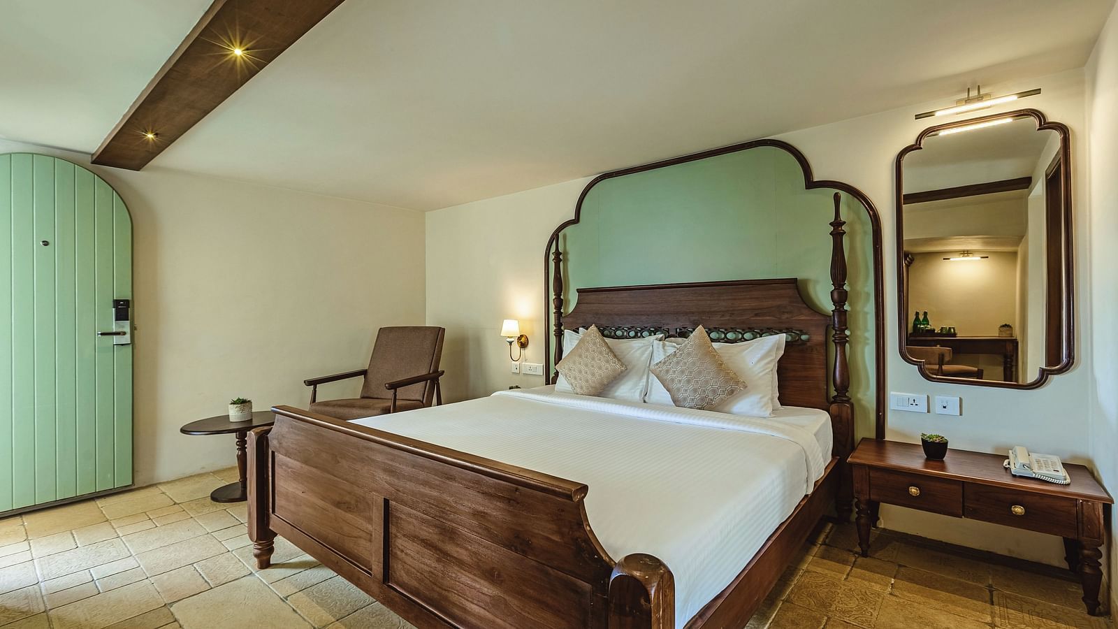 Well-lit bedroom at Mango Hill Shola, Ooty featuring a double bed with a pastel green headboard, wooden flooring, and cosy seating.