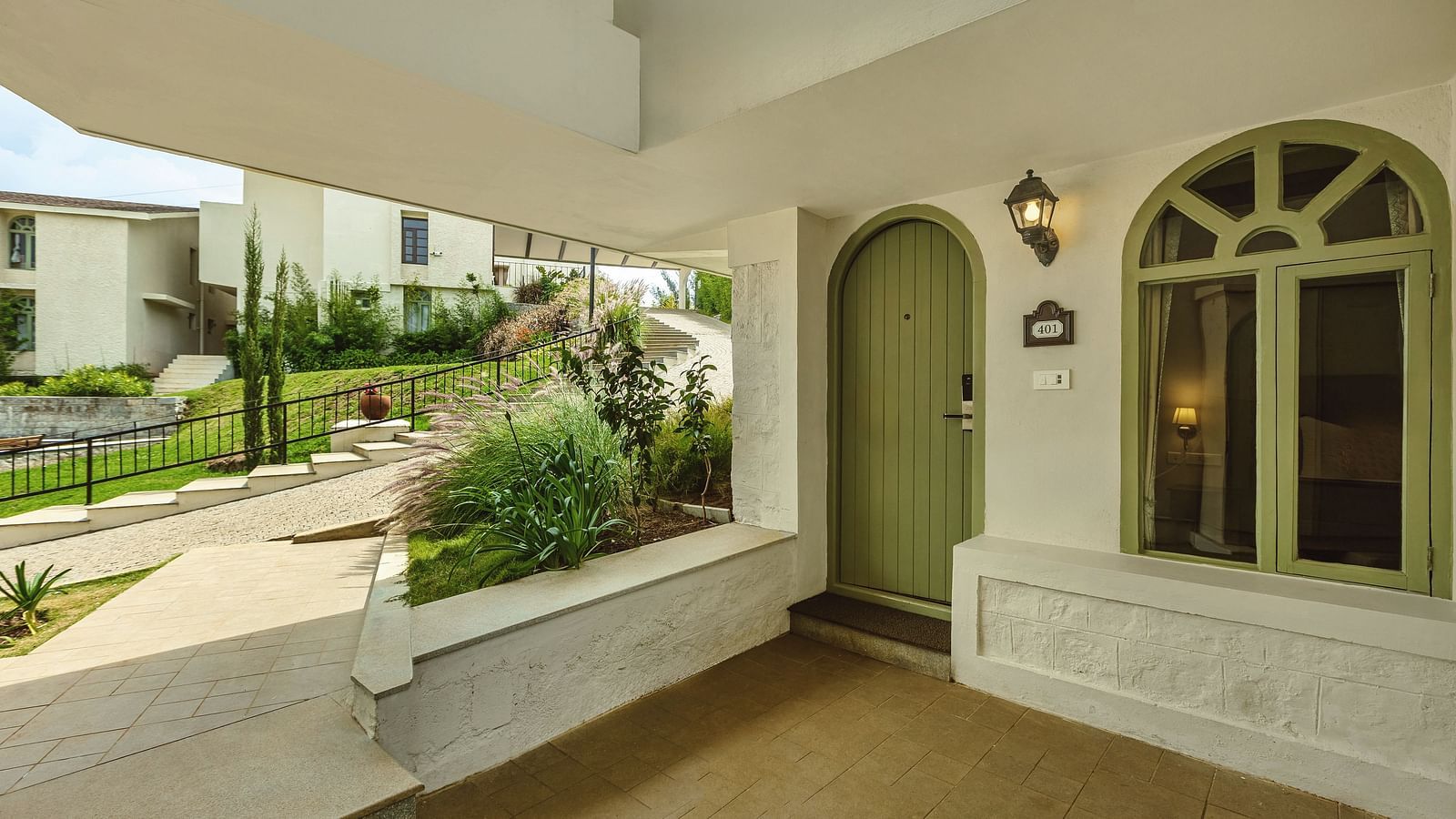 Exterior view of a cottage-style room entrance at Mango Hill Shola, Ooty with arched doors, stucco walls, and garden walkway.