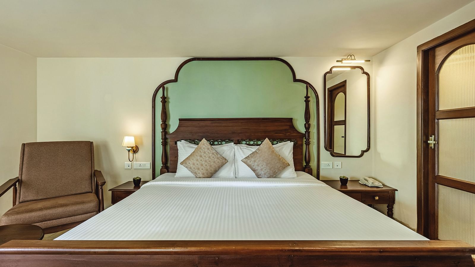 Front-facing view of the bed at Mango Hill Shola, Ooty with pastel green headboard, warm lighting, and a classic wooden design.