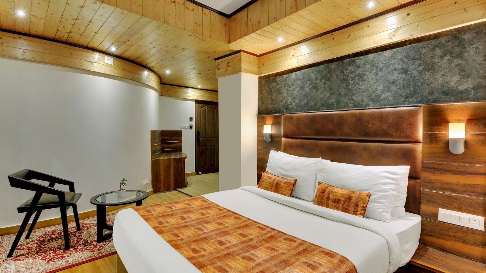 An image of Sumitel Queensyard deluxe room with king size bed, a chair and a table and minimal decoration