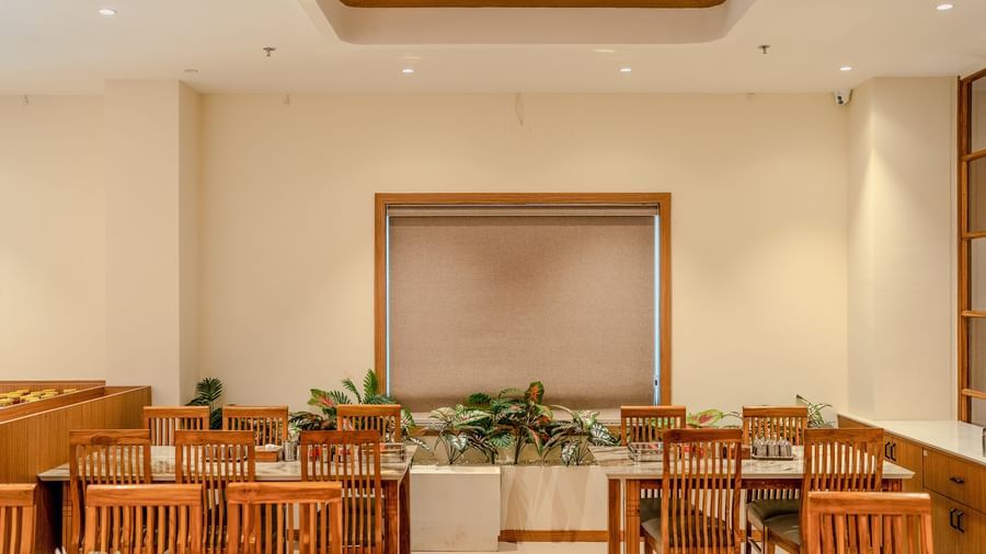 A window with brown-coloured blinds covering it along with well-arranged dining setup at Daksh The Grand Goverdhan, Dwarka.