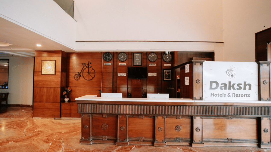 The hotel reception desk with a dark wood finish and a marble-effect floor at Daksh The Madhuvan Suites, Dwarka.