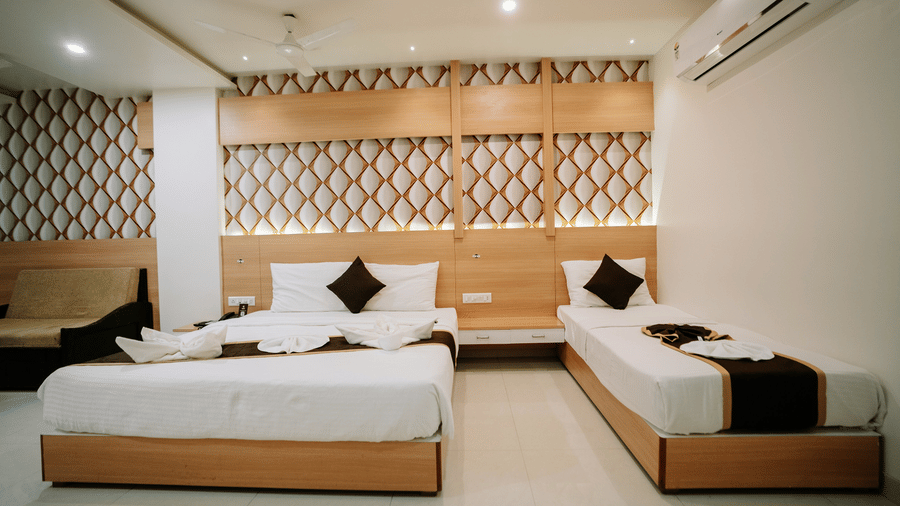 Bright hotel room with a large bed, decorative lattice-patterned wooden headboard, white bedding, and towel art at Daksh The Madhuvan Suites, Dwarka.